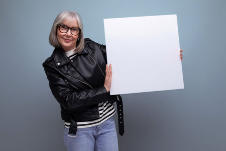 confident mature woman with gray hair demonstrates mockup banner on bright background with copy spaceの写真素材