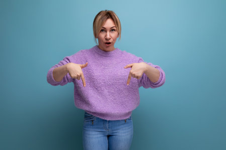 portrait of an indignant sad blonde young woman in a lavender sweater on a bright plain backgroundの写真素材