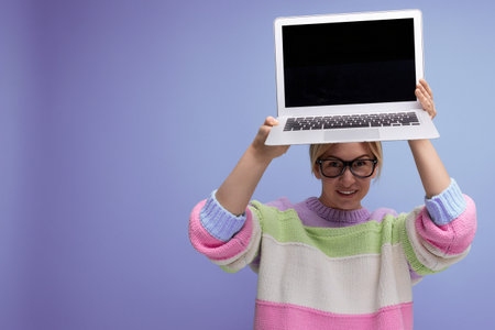 nice blond woman freelancer with a laptop in her hands shows a screen mockup on a purple backgroundの写真素材
