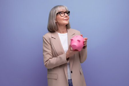 cute old woman in a jacket with a piggy bank of money savings on a bright background with copy spaceの写真素材