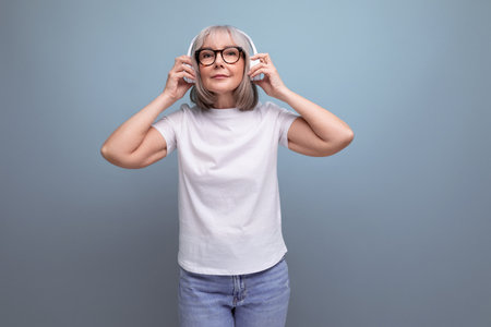 middle age business. mature lady with gray hair listens to music in wireless headphones on studio...
