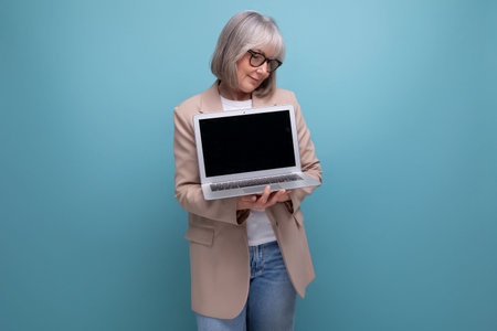 close-up of a confident 60s middle-aged woman in a jacket with a laptop on a bright background with copy spaceの写真素材