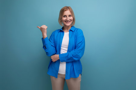close-up of a joyful middle aged woman in a blue shirt on a blue background with copy spaceの写真素材