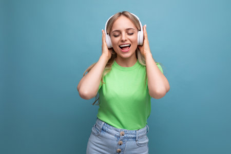 adorable blond girl in casual outfit dancing to music in big white headphones on a blue backgroundの写真素材
