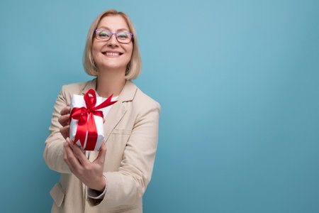 middle-aged business concept. a woman in a jacket holds a gift box with a bow on a studio background with copy spaceの写真素材