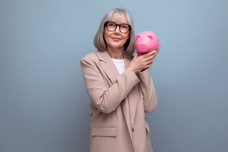pleasant 60s middle-aged woman with a piggy bank of money on a bright background with copy spaceの写真素材