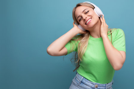 close-up of an adorable blond girl in a casual outfit relaxing and dancing in big white headphones on a blue backgroundの写真素材