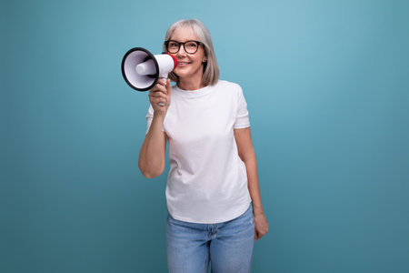 portrait of a woman of mature years with gray hair with a loudspeaker on a studio background with copy spaceの写真素材
