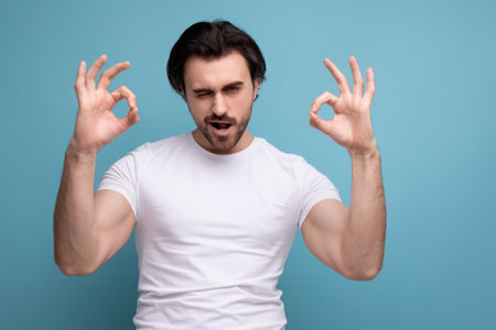 confident young brutal brunette man in a white t-shirt and jeans shows class with his handの写真素材