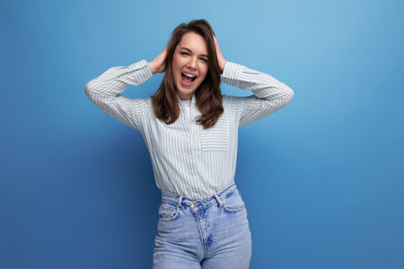 well-groomed young brunette lady dressed in a striped shirt and jeans smiling on a studio backgroundの写真素材