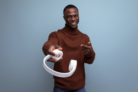 positive young african male consultant holding out headphones to the camera on the background with copy spaceの写真素材