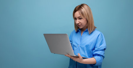 attentive millennial woman in casual shirt holding a laptop in her hands on a blue isolated background with copy spaceの写真素材