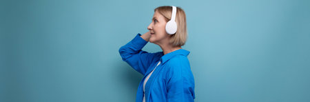 middle age business concept. mature woman listening to audiobook with headphones on blue background...
