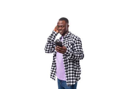 handsome young african man with short haircut in plaid shirt chatting on social network in smartphoneの写真素材