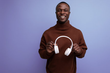 positive young african male consultant holding out headphones to the camera on the background with...