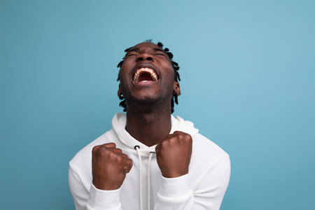 joyful winner african 20s man with dreadlocks on background with copy space