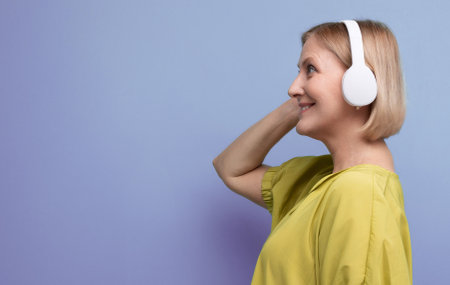smiling blond mature woman listening to podcast in headphones wirelesslyの写真素材