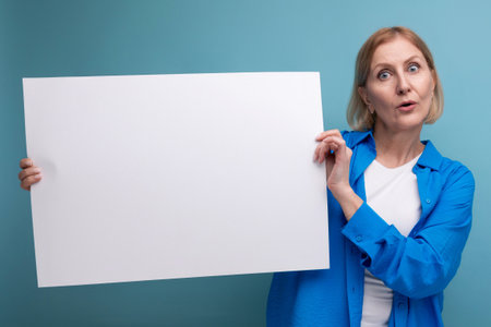 middle age business concept. middle-aged woman holding a poster for notes with a mocap on a blue background copy spaceの写真素材