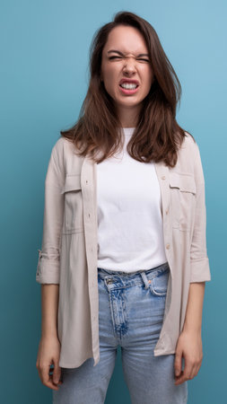 cheerful cute brunette young brunette lady dressed in a shirt and jeans with a grimace on her faceの写真素材