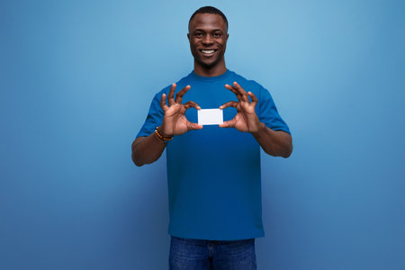young american guy dressed in a basic t-shirt holding a plastic card on the background with copy...