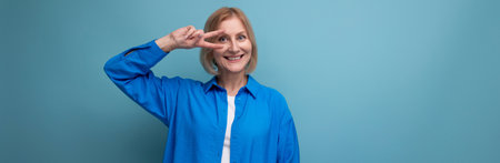 close-up of a charming mature woman in a blue shirt on a blue background with copy spaceの写真素材
