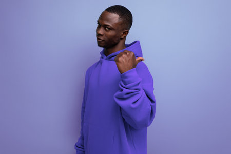 cheerful cute ethnic 25 year old african man in a stylish hoodie with a hood on a blue backgroundの写真素材