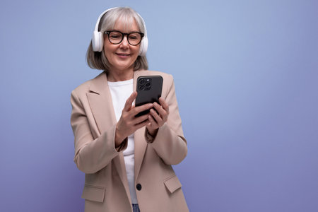 trendy 60s woman in a stylish jacket listens to music in big headphones on a bright background with...