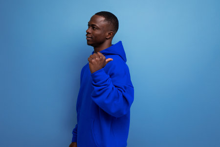 stylish cool young guy american with dark skin is dressed in a trendy sweatshirt with a hood on a studio background with copy spaceの写真素材