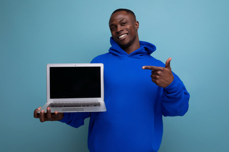 handsome african young consultant in stylish hoodie with laptop to show ads on background with copy spaceの写真素材
