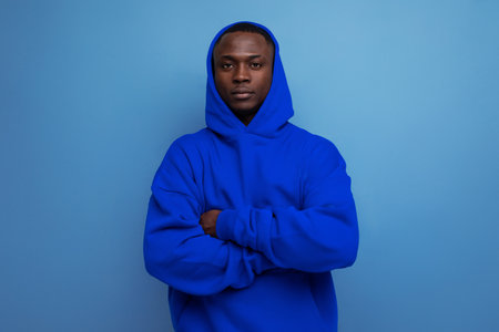 stylish cool young guy american with dark skin is dressed in a trendy sweatshirt with a hood on a studio background with copy spaceの写真素材