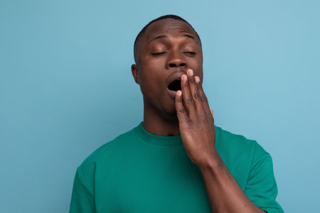young american man in t-shirt yawns on blue background with copy space. people lifesal conceptの写真素材