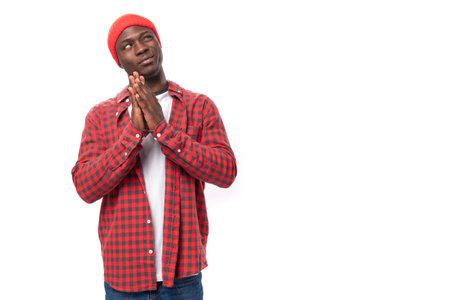 portrait of a dreamy modest 30s black american man dressed in a red shirt and cap on a white studio...