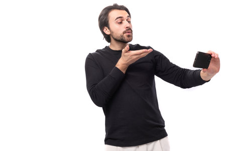 young handsome brunet european man in black sweatshirt talking by video link on isolated white backgroundの写真素材