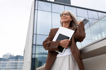 beautiful successful mature business woman with gray hair with documents in her hands stands against the backdrop of a business centerの写真素材