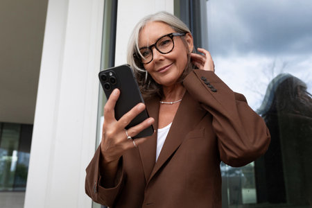 beautiful gray-haired successful mature business woman enjoys checking messages on smartphoneの写真素材