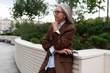 charming mature woman with gray hair in a stylish suit walks around the cityの写真素材