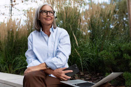 close-up of a slender well-groomed pretty gray-haired business woman pensioner against the background of greeneryの写真素材