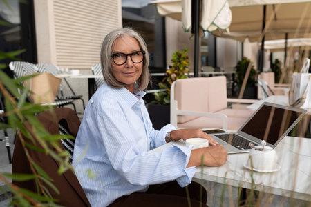 slender cute gray-haired entrepreneur woman of mature years in a light shirt is resting during a...