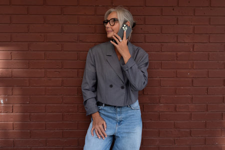 successful confident middle-aged woman dressed in a gray stylish jacket walks down the street and...