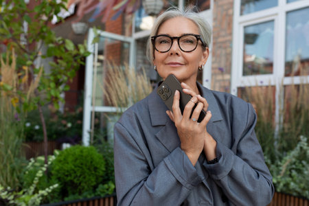 gray-haired mature dreamy woman dressed in a stylish gray jacket and jeans walks and enjoys the...