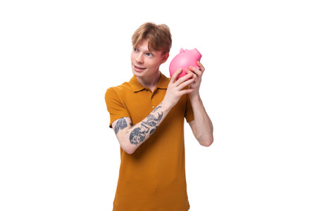 young man with red hair in an orange t-shirt holding a piggy bankの写真素材