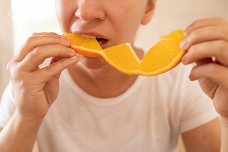 Young woman feels hungry and eats orange at breakfastの写真素材