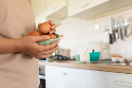 A woman holds chicken eggs in a bowl while standing in the kitchenの写真素材