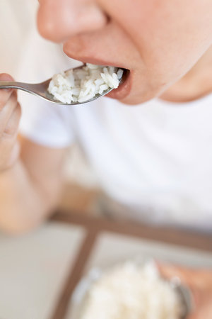 young woman brings a spoon of rice to her mouthの写真素材