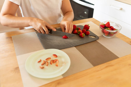 a woman slices strawberries with a knife in the kitchen