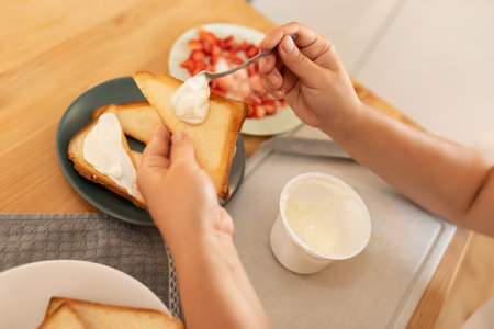 top view, a woman spreads sour cream on toast and puts strawberries on itの写真素材