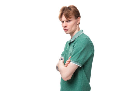 a young slender ginger man with a tattoo on his arm, dressed in a green T-shirt stands sideways
