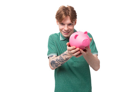 a young red-haired caucasian guy in a green t-shirt is about to empty his piggy bankの写真素材