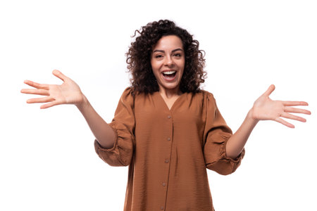 portrait of a young assistant curly brunette woman dressed in a brown shirt on a white background with copy spaceの写真素材
