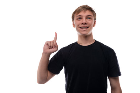 Positive teenager guy in a black T-shirt holds his index finger up on a background with copy spaceの写真素材